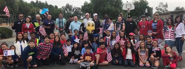 Photo of several elementary students and school staff memvbers with military veterans. Several of them have American flags.